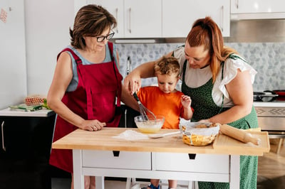 familia cocinando, mujer mayor junto a mujer joven y niño cocinando un pastel