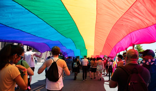 salud-integral-de-comunidad-lgbt-guia-para-profesionales-de-la-salud-personas-marchando-por-el-orgullo-debajo-de-una-bandera-arcoiris-en-la-ciudad-de-san-diego