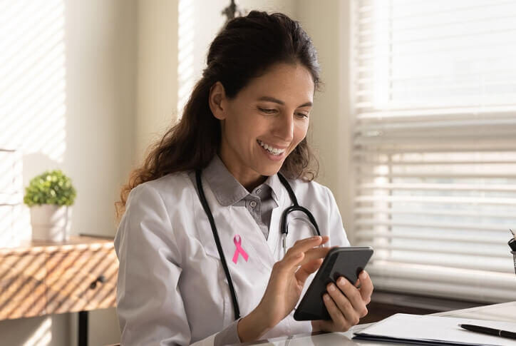 octubre rosa, doctora con un moño rosa en su bata, sonriendo mientras revisa su teléfono