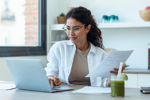 female-latin-american-adult-doctor-consultation-room-working-on-laptop-while-holding-documents-web