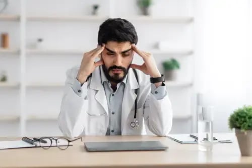 ia en medicina, doctoralia connect, médico con barba y dolor de cabeza sentado frente al escritorio