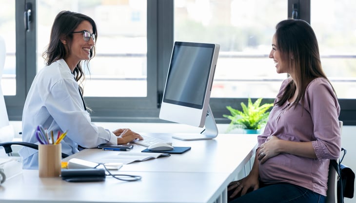 Pretty-young-woman-gynecologist-reviewing-the-medical-history-of-her-pregnant-patient-with-computer-in-the-clinic.-1174584743_1360x775